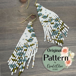 Op de afbeelding: Een paar witte, groene en gouden kralen oorbellen met een franje ontwerp. De oorbellen zijn handgemaakt en hebben een geometrisch patroon. De oorbellen zijn gelabeld "Original Pattern by Opal & Olive Designs".