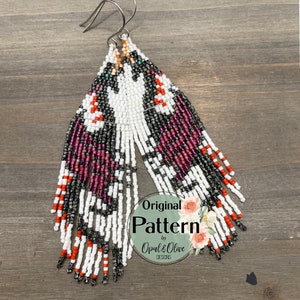 Könnte beinhalten: Ein Paar lange, geperlte Ohrringe mit einem geometrischen Muster in Weiß-, Schwarz-, Rot- und Lilatönen. Die Ohrringe sind aus Perlen gefertigt und haben ein fransigen Design. Die Ohrringe sind mit "Original Pattern by Opal & Olive Designs" gekennzeichnet.