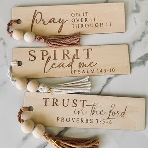 May include: Three wooden bookmarks with inspirational quotes and scripture verses. The bookmarks have tassels and wooden beads. The quotes are "Pray on it over it through it", "Spirit lead me Psalm 143:10", and "Trust in the Lord Proverbs 3:5-6".