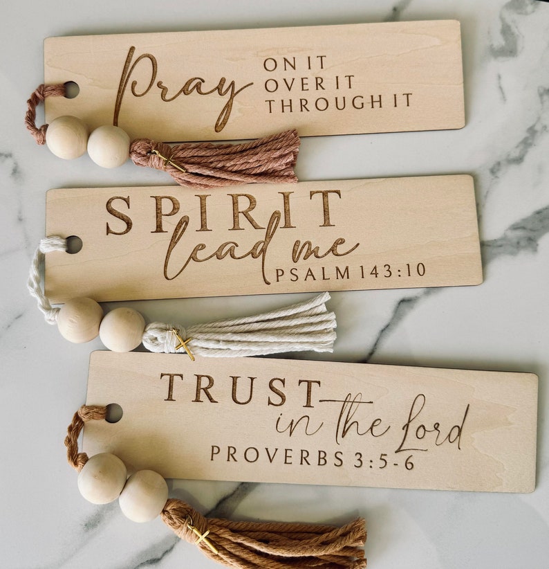 May include: Three wooden bookmarks with inspirational quotes and scripture verses. The bookmarks have tassels and wooden beads. The quotes are "Pray on it over it through it", "Spirit lead me Psalm 143:10", and "Trust in the Lord Proverbs 3:5-6".
