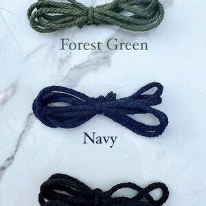 May include: Three spools of cord in different colors: forest green, navy blue, and black. The cords are arranged in a figure eight shape.