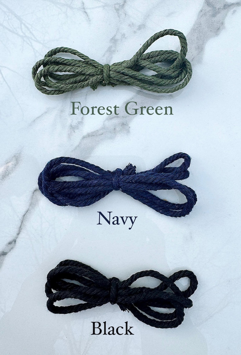 May include: Three spools of cord in different colors: forest green, navy blue, and black. The cords are arranged in a figure eight shape.