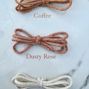 May include: Three spools of natural fiber rope in different colors: coffee, dusty rose, and natural. The rope is twisted and has a rough texture.