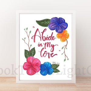 Op de afbeelding: Een witte ingelijste print met een bloemenontwerp en de tekst "Abide in my love" met de bijbelverwijzing "Johannes 15:9".
