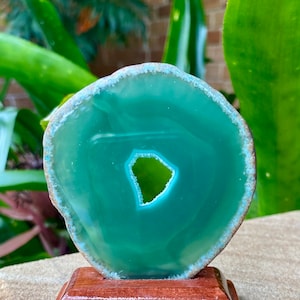 May include: A green agate slice with a natural hole in the center, displayed on a wooden stand.