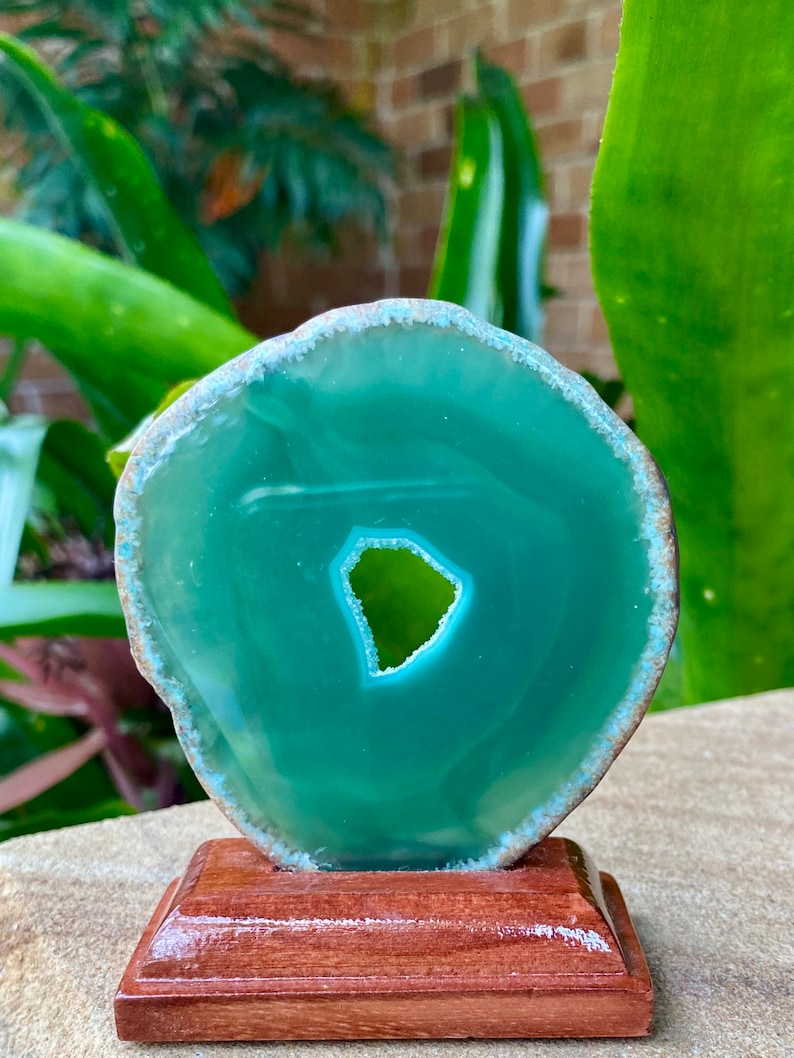 May include: A green agate slice with a natural hole in the center, displayed on a wooden stand.