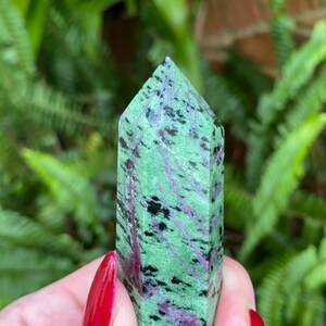 May include: A green, pink, and black zoisite crystal point. The crystal is smooth and polished, with a pointed tip.