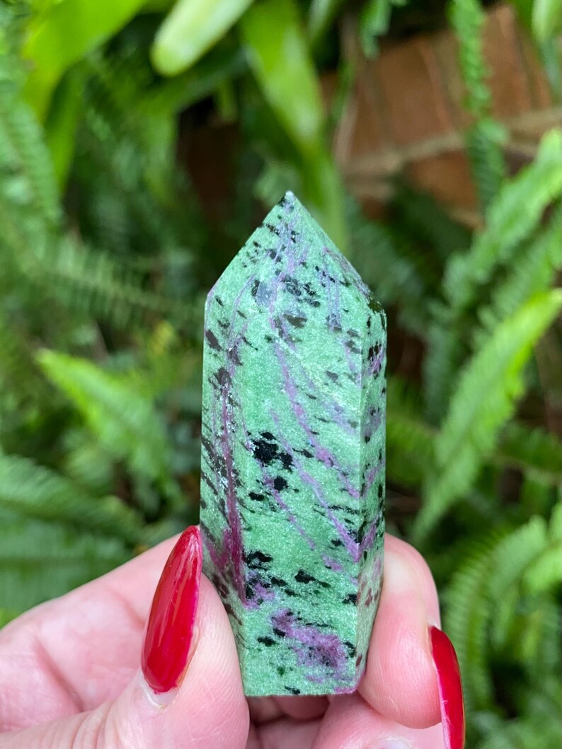 May include: A green, pink, and black zoisite crystal point. The crystal is smooth and polished, with a pointed tip.