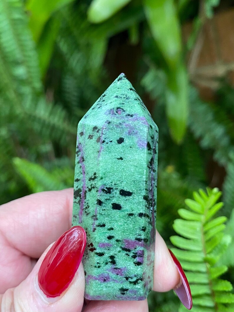 May include: A green, black, and purple gemstone point with a pointed tip. The gemstone is smooth and polished.