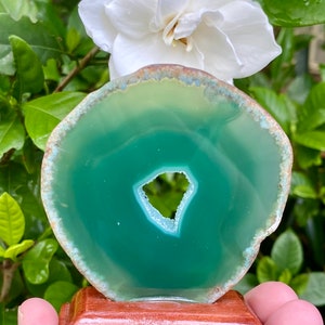 May include: A green agate slice with a natural hole in the center, displayed on a wooden stand.