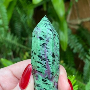 May include: A green, black, and pink crystal point with a pointed tip. The crystal is smooth and polished.
