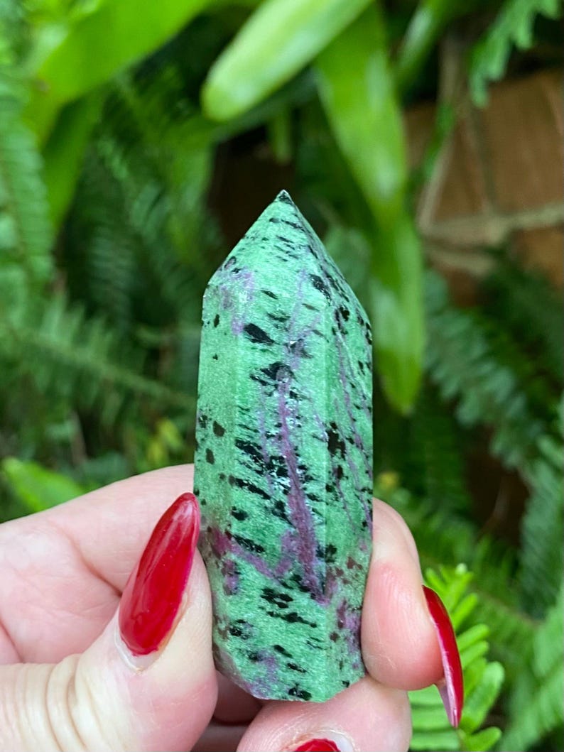 May include: A green, black, and pink crystal point with a pointed tip. The crystal is smooth and polished.