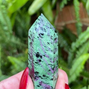 May include: A green, black, and purple gemstone point with a smooth, polished finish. The point is approximately 2 inches tall and is a popular choice for crystal healing and meditation.