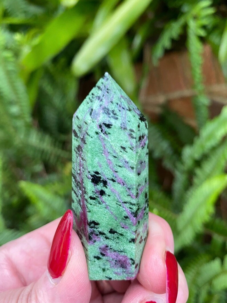 May include: A green, black, and purple gemstone point with a smooth, polished finish. The point is approximately 2 inches tall and is a popular choice for crystal healing and meditation.