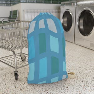 May include: A tall, cylindrical laundry bag featuring a repeating grid pattern in shades of light blue, medium blue, and teal. The bag has a drawstring closure at the top and is constructed from fabric, standing upright with a structured, rounded shape.