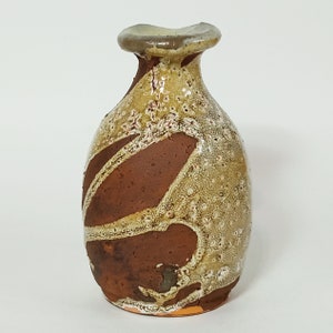 May include: A small, brown and white ceramic vase with a textured surface. The vase has a wide mouth and a narrow neck.
