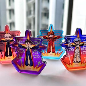 Op de afbeelding: Vier kleurrijke acryl bedels met anime-personages in een kruisvormig ontwerp. Elke bedel heeft een ander personage in een unieke outfit, met oog- en vlamdetails. De bedels zijn in tinten roze, paars, blauw en oranje.