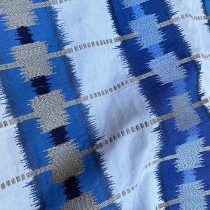 May include: Close-up of a fabric with a repeating pattern of blue, gray, and white vertical stripes. The stripes have a textured, woven appearance with a mix of solid and dotted lines. The fabric is likely cotton or linen.