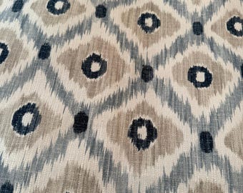 May include: Close-up of a fabric with a repeating pattern. The design features diamond shapes in shades of beige, blue, and white, with dark blue circular accents. The fabric has a textured appearance, suggesting a woven material.