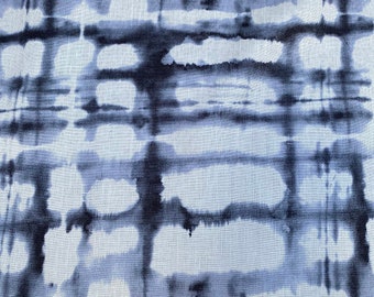 May include: Close-up of a fabric with a tie-dye pattern. The design features a grid-like arrangement of dark blue and light blue shapes against a white background. The fabric has a textured appearance.