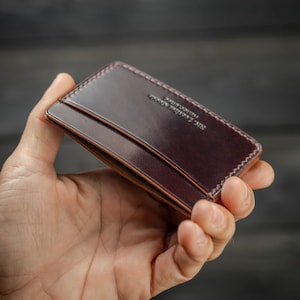 May include: A dark brown leather cardholder with a stitched border. The cardholder has a sleek design with a slot for cards and the text "R.C. Leather Goods" embossed on the surface.