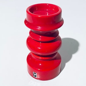 Könnte beinhalten: Ein roter Kerzenhalter aus Keramik mit einem strukturierten Design. Der Halter hat eine breite Basis und eine schmale Oberseite mit einer kleinen Öffnung für eine Kerze.