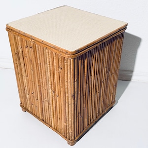 Könnte beinhalten: Ein quadratischer, geflochtener Bambus-Aufbewahrungskorb mit einem cremefarbenen Stoffdeckel. Der Korb hat eine natürliche Holzoptik und ist perfekt zum Verstauen von Decken, Spielzeug oder anderen Haushaltsgegenständen.