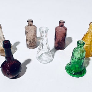 Könnte beinhalten: Eine Sammlung von sechs antiken Glasflaschen in verschiedenen Farben und Formen. Die Flaschen sind alle klein und haben ein einzigartiges, antikes Aussehen.