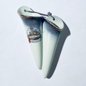 Könnte beinhalten: Zwei weiße Keramik-Blumenvasen mit goldener Verzierung. Die Vasen sind kegelförmig und haben oben ein kleines Loch zum Aufhängen. Die Vase links hat ein gemaltes Bild eines Schlosses mit dem Text "Cochem Burg Cochem".