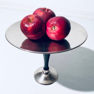 Könnte beinhalten: Drei rote Äpfel auf einem silbernen Kuchenständer mit schwarzem Fuß.