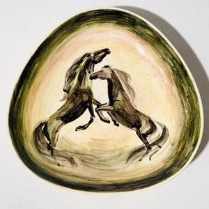May include: A ceramic serving dish with a hand-painted design of two rearing horses. The horses are depicted in shades of brown and black against a cream-colored background, framed by a green and pink border.