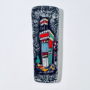 May include: A black and white ceramic tile with a colourful illustration of a building with the text "S. MARINO" at the bottom.