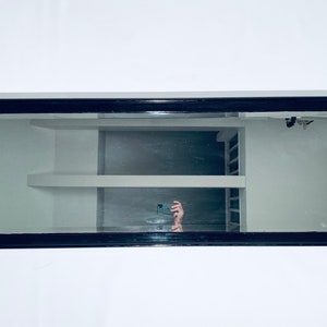 Könnte beinhalten: Ein schwarzer Spiegel mit einem Spiegelbild eines Raumes mit weißen Regalen. Die Regale sind leer.