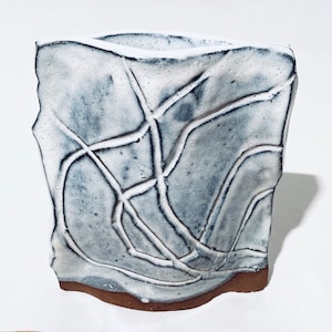 Könnte beinhalten: Weiße Keramikvase mit einem strukturierten, abstrakten Design in Grautönen. Die Vase hat eine leicht unregelmäßige Form und einen braunen Boden.