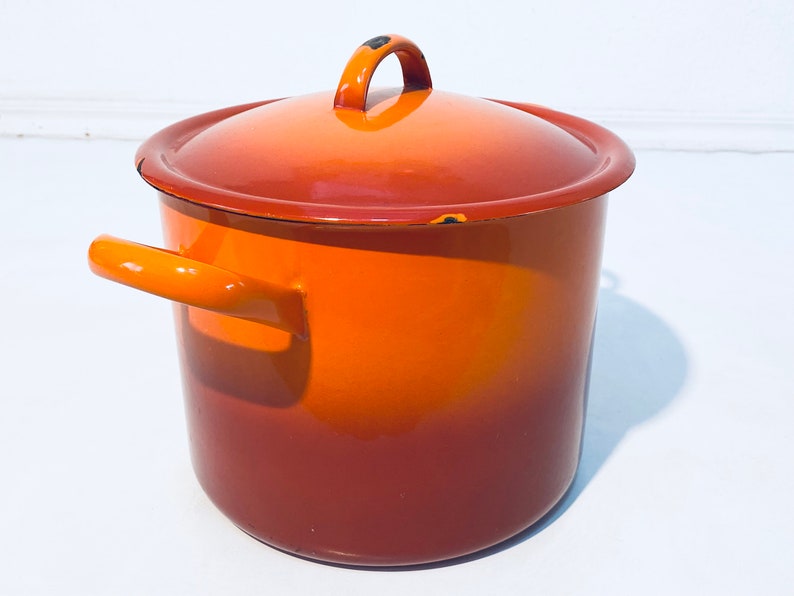 Pu&ograve; includere: Una pentola smaltata arancione e marrone con un coperchio e un'unica maniglia. La pentola ha un gradiente di colore dall'arancione al marrone.