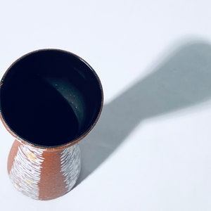 Puede incluir: Un jarr&oacute;n de cer&aacute;mica marr&oacute;n con un patr&oacute;n geom&eacute;trico blanco y amarillo. El jarr&oacute;n tiene un interior esmaltado negro.