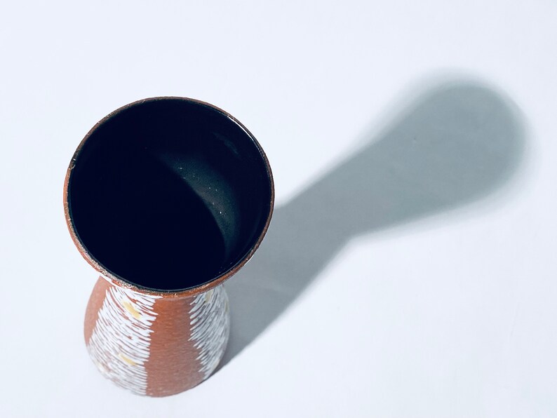 Puede incluir: Un jarr&oacute;n de cer&aacute;mica marr&oacute;n con un patr&oacute;n geom&eacute;trico blanco y amarillo. El jarr&oacute;n tiene un interior esmaltado negro.