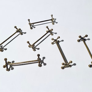 Könnte beinhalten: Sechs Besteckhalter aus goldenem Metall mit geometrischem Design. Jeder Halter hat eine lange, dünne Stange mit abgerundetem Ende und eine Basis mit fünf abgerundeten Punkten.