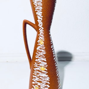 Puede incluir: Un jarr&oacute;n de cer&aacute;mica marr&oacute;n con un patr&oacute;n geom&eacute;trico blanco y amarillo. El jarr&oacute;n tiene una abertura acampanada y un asa.