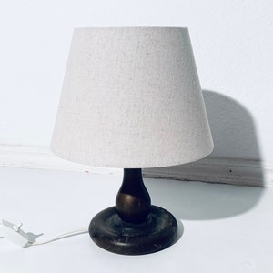 May include: A wooden table lamp with a white linen shade. The lamp has a dark brown wooden base with a rounded shape.