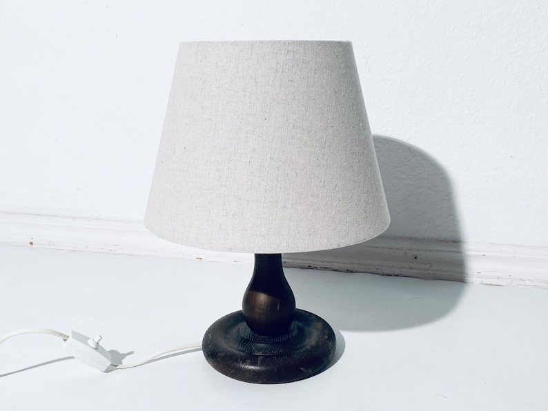 May include: A wooden table lamp with a white linen shade. The lamp has a dark brown wooden base with a rounded shape.