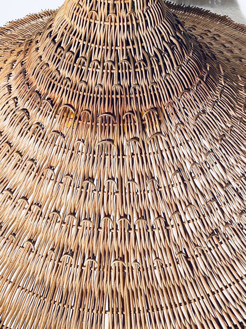 May include: Close-up of a woven wicker lampshade in a natural brown colour. The lampshade is made of thin, tightly woven strips of wicker, creating a textured and intricate pattern.