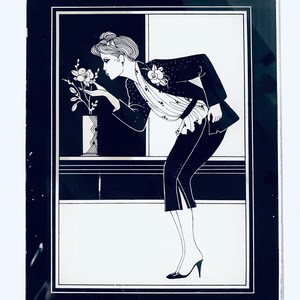 May include: A black and white illustration of a woman in a black jacket and skirt, smelling a flower in a vase. The image is framed in a black frame.