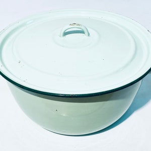 Könnte beinhalten: Ein weißer Emailletopf mit Deckel und dunkelgrünem Rand. Der Topf hat an jeder Seite einen Griff und einen kleinen Griff am Deckel.