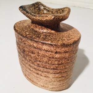 Może przedstawiać: Mały, brązowy wazon ceramiczny z fakturowaną, falistą powierzchnią i szerokim, płaskim otworem. Wazon ma brązową glazurę w kropki z ciemniejszymi brązowymi akcentami.