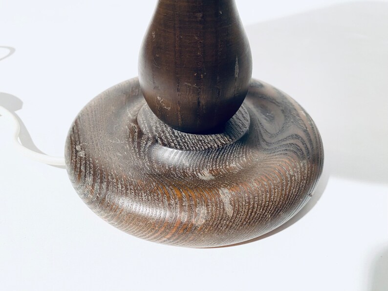 May include: A dark brown wooden table lamp base with a rounded, bulbous shape. The base has a smooth, polished finish and a slightly textured surface.