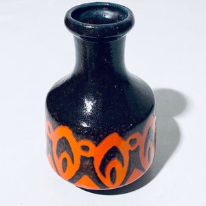 Puede incluir: Un jarrón pequeño de cerámica marrón oscuro con un diseño geométrico naranja y negro alrededor de la base.