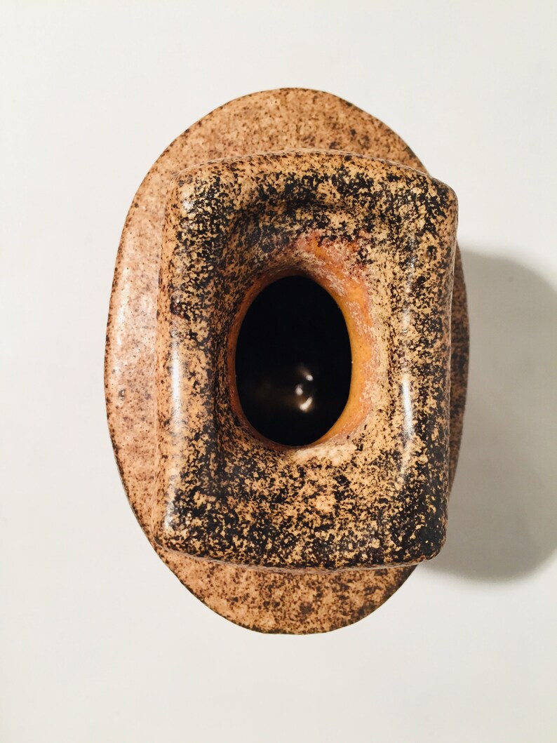 Może przedstawiać: Brązowy i czarny ceramiczny wazon z kwadratowym otworem. Wazon ma pstrokatą glazurę.