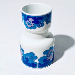 Könnte beinhalten: Eine weiße Keramikvase mit einem blauen und violetten Blumenmuster. Die Vase hat einen schmalen Hals und einen breiteren Boden.