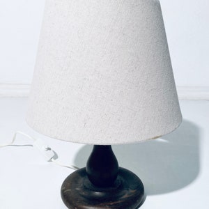 May include: A wooden table lamp with a white fabric lampshade. The lamp has a dark brown wooden base with a round, flat top and a bulbous, rounded stem.